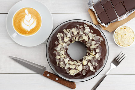 Homemade chocolate cheesecake with almond slices and cup of coffee cappuccino on white wooden table....