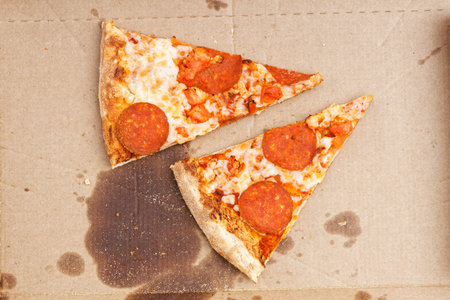 Closeup leftover two pieces of pizza with pepperoni and tomatoes in a cardboard box. Top view.