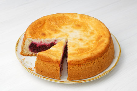 Closeup homemade raspberry pie and sliced piece on white wooden table.