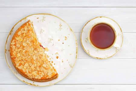Half of homemade gooseberry pie garnished with almond petals and cup of tea on white wooden table. Top view.の写真素材