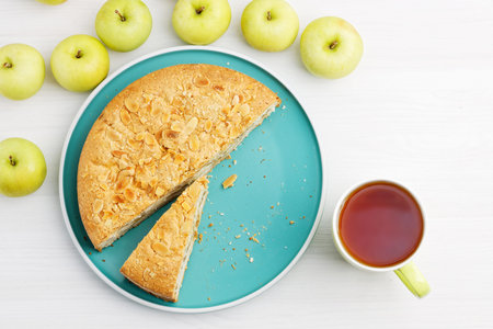 Homemade pastry. Apple pie with almond petals and cup of tea on white wooden table. Top view.