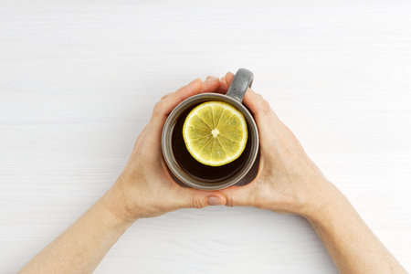 Female hands hold a warm cup of tea with a slice of lemon. Top view
