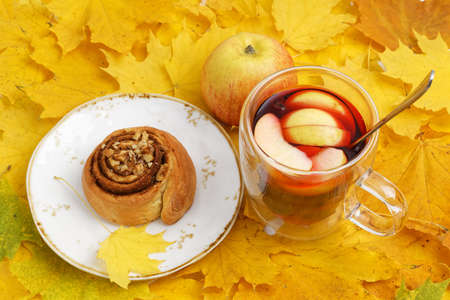 Homemade cinnamon bun and a mug of mulled wine on a pile of yellow autumn leavesの写真素材