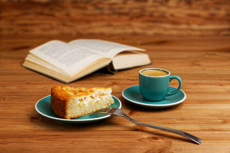 Piece of apple pie, cup of coffee espresso and open book on wooden table. Shallow focus.の写真素材