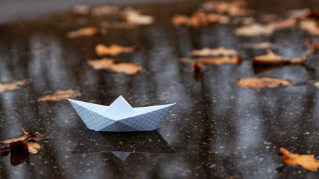 Paper boat floating on the water of an autumn puddle among fallen leaves. Shallow focus.の写真素材