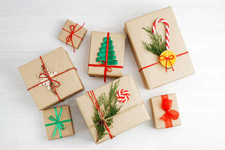 Group of gift boxes wrapped in kraft paper, tied with twine and decorated with a ribbons on white wooden table.の写真素材