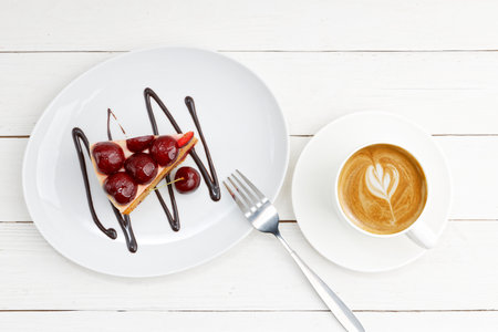 Closeup piece of homemade cake with cherries and cup of coffee cappuccino on white wooden table. Top view.の写真素材