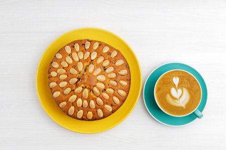 Homemade cake with almonds and cup of coffee cappuccino on a white wooden table. Top view.