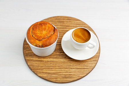 Homemade cinnamon bun from yeast dough in white ceramic mold and cup of coffee espresso on round...