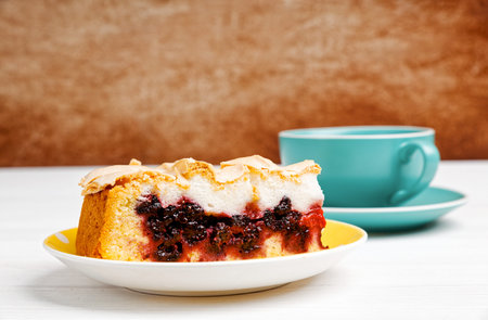 Piece of homemade berry cake with meringue and cup of tea on white wooden table. Copyspace.