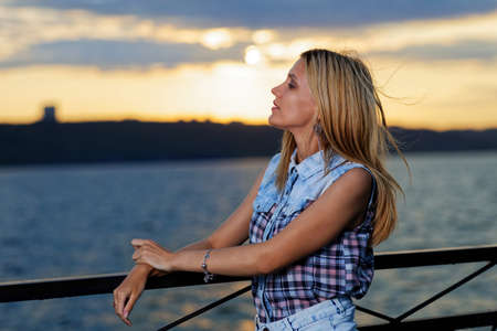 Portrait of a girl on the embankment of the river on the sunset backgroundの写真素材