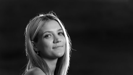 Portrait of a young attractive girl in backlight against dark blurred background. Black and white....