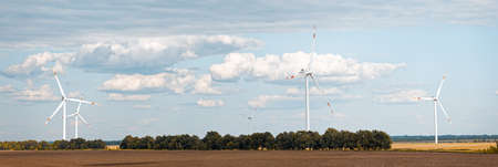 Rotating wind generators in the field against the cloudy sky on sunny summer day. Panoramic view.の写真素材