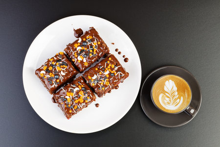 Homemade brownie and cups of coffee cappuccino on dark table. Top view.