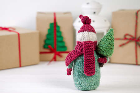 Handmade knitted gnome with Christmas tree on white wooden table against gift boxes on blurred background. Christmas concept.の写真素材