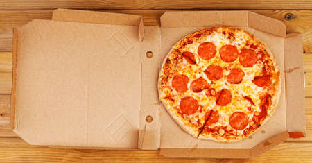 Open box with pepperoni pizza on wooden table. Top view.の写真素材