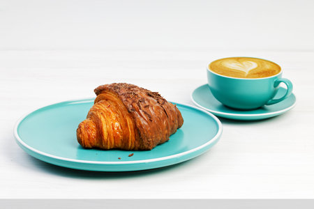 Croissant with chocolate and cup of coffee cappuccino on white wooden table.の写真素材
