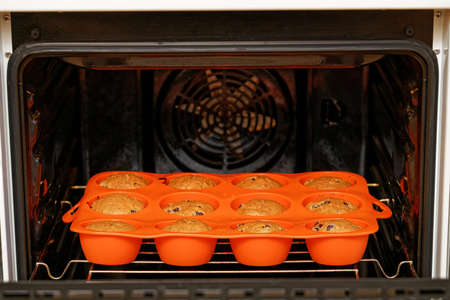 Homemade cherry cupcakes baked in a red silicone mold inside a home oven. Shallow focus.の写真素材