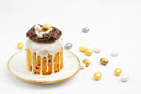 Homemade Easter cake decorated with candies in the form of Easter eggs on white wooden table.