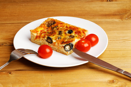 Piece of homemade cheesy Quiche with tomatoes, champignons and olives. close-up view.