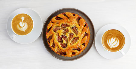 Closeup homemade fig pie and two cups of coffee cappuccino on white wooden table. top view.