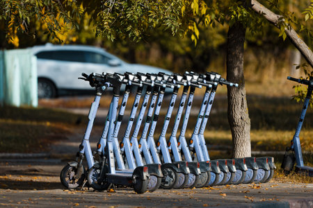 A row of shared electric scooters parked on a sidewalk in a city during autumn. The scene, with...