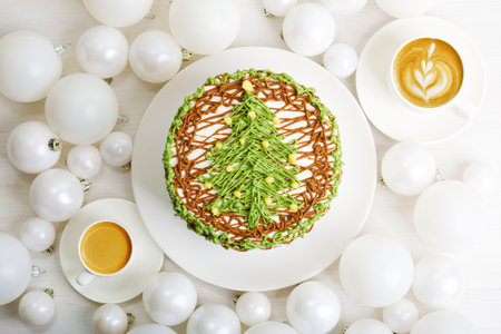 Homemade cake decorated with Christmas tree, two cups of coffee and Christmas balls on white wooden table. Top view.の写真素材
