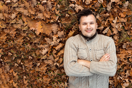 Autumn season, happiness and people concept - smiling young man lying on the ground or grass and fallen leaves in autumn park. Concept of autumn, autumn mood. Copy space.の写真素材