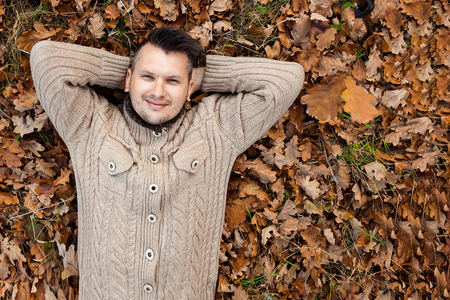 Autumn season, happiness and people concept - smiling young man lying on the ground or grass and fallen leaves in autumn park. Concept of autumn, autumn mood. Copy space.の写真素材