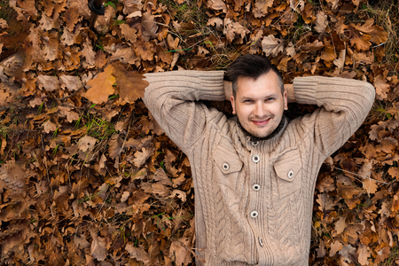 Autumn season, happiness and people concept - smiling young man lying on the ground or grass and fallen leaves in autumn park. Concept of autumn, autumn mood. Copy space.の写真素材