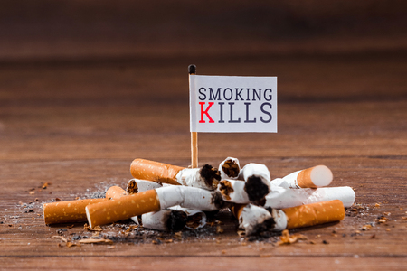Creative background. A pile of cigarette butts on a wooden background, the inscription smoking kills. The concept of smoking kills, nicatine poisons, cancer from smoking, stop smoking. Copy space.の写真素材