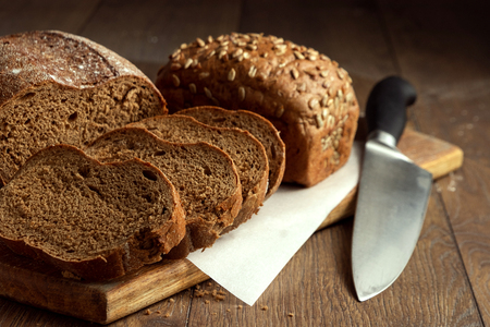 Creative background, sliced rye bread and a knife close-up, on a wooden cutting board, flat lay, copy space. The concept of fresh pastry, black bread.の写真素材