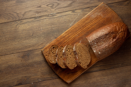 Creative background, freshly baked sliced rye bread on a wooden cutting board, flat lay, copy space. The concept of fresh pastry, black bread.の写真素材