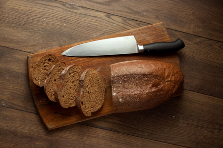 Creative background, sliced rye bread and a knife close-up, on a wooden cutting board, flat lay, copy space. The concept of fresh pastry, black bread.の写真素材