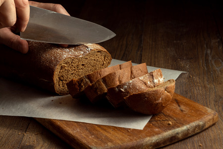 Creative background, male hands cut rye bread close-up, on a wooden cutting board, flat lay, copy space. The concept of fresh pastry, black bread.の写真素材