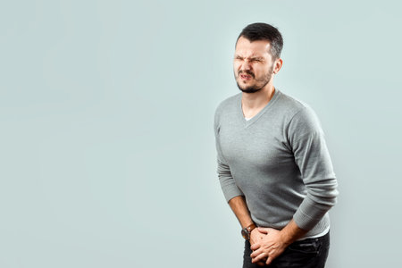 A young, attractive man feels pain in his groin, arms folded between his legs. Experiencing pain,...