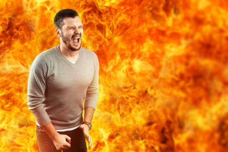 A young attractive man feels pain in a flame, surrounded by hot fire. He feels hate, anger, anger,...
