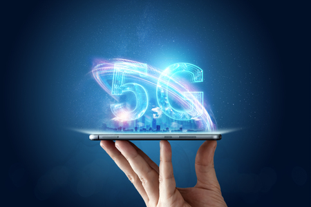 Creative background, male hand holding a phone with a 5G hologram on the background of the city. The concept of 5G network, high-speed mobile Internet, new generation networks. Copy space, Mixed media.の写真素材
