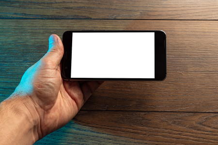 Closeup male hands holding smartphone with white screen, against the background of a wooden table. Concept of blank, mobile games, mockup, layout, copy space.の写真素材