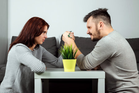 Husband and wife are fighting in their arms, arm wrestling between male and female. Family quarrel,...