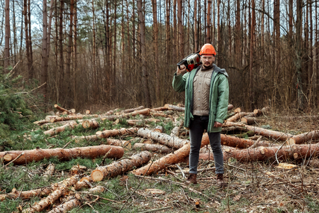 Logging, Worker in a protective suit with a chainsaw. Cutting down trees, forest destruction. The concept of industrial destruction of trees, causing harm to the environment.の写真素材