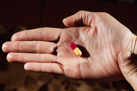 Closeup of a female's hand holding a white pill. The concept of illness, medication, the cost of medicines.の写真素材