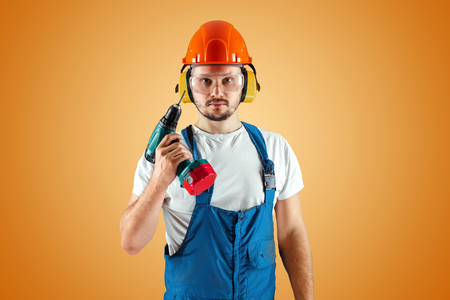A male construction worker in an orange helmet holds a screwdriver on an orange background. Construction concept, contractor, repair.の写真素材