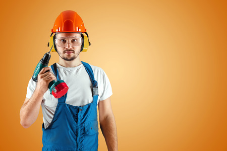 A male construction worker in an orange helmet holds a screwdriver on an orange background. Construction concept, contractor, repair.の写真素材