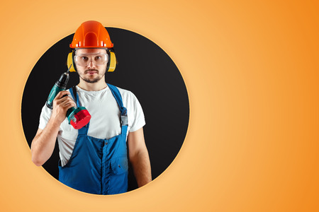 A male construction worker in an orange helmet holds a screwdriver on an orange background. Construction concept, contractor, repair.の写真素材