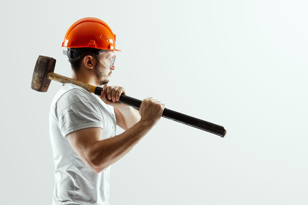 Male builder in orange helmet with sledge hammer isolated on white background. Concept building, contractor.の写真素材