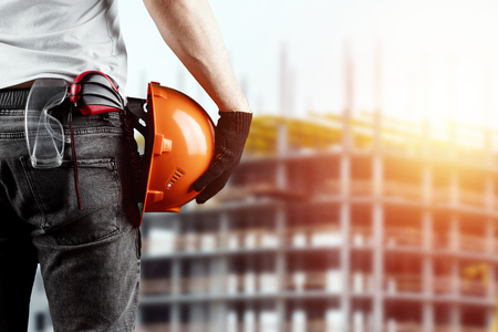 A builder, an architect holds in his hand a construction helmet against the background of a construction site, a tape measure. Concept architecture, construction, engineering, design, repair.の写真素材