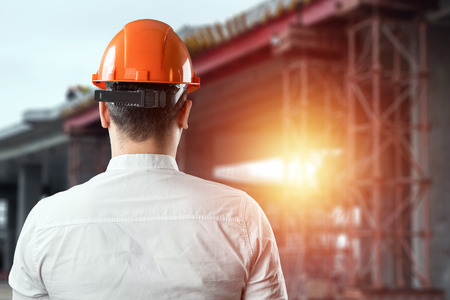 Portrait of a man from behind in a construction, orange helmet against the background of a construction site. Concept architecture, construction, engineering, design, repair. Copy spaceの写真素材