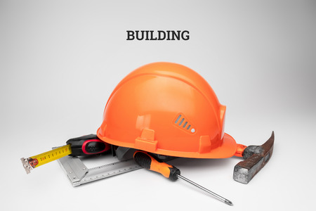 White construction helmet, tape measure, hammer, screwdriver on a light background. Inscription construction. Concept architecture, construction, engineering, design, repair.の写真素材