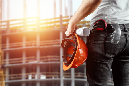 A builder, an architect holds in his hand a construction helmet against the background of a construction site, a tape measure. Concept architecture, construction, engineering, design, repair.の写真素材